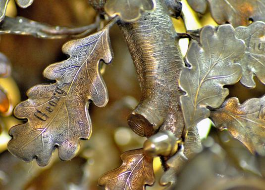 Tuvplāns ar metāla ozollapu skulptūru, kuras lapās iegravēti vārdi un detaļas atgādina dabas faktūru.