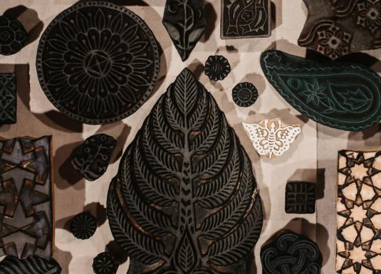 Uz galda izvietoti dažādu formu un rakstu koka spiedogi tekstila apdrukai.