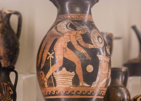 Antīkie grieķu keramikas trauki ar sarkanfigūru gleznojumiem, izstādīti vitrīnā.
