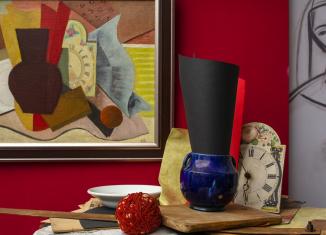 Klusās dabas glezna ar vāzi un pulksteni, papildināta ar reāliem priekšmetiem izstāžu telpā.